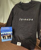 Black long sleeved tee shirt and box set of F.R.I.E.N.D.S DVDs showing the logo on the shirt and box