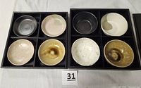 Top view showing eight small ceramic Japanese dishes arranged in two dark wooden divided boxes with four dishes per box.