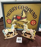 Front view of framed Merry-Go-Round sign with two wooden carousel horses placed in front.
