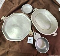 Display of four metal serving items: 13-inch octagon hammered aluminum tray, oval hammered aluminum plate, cast iron pewter porridge bowl, and a small round metal dish.