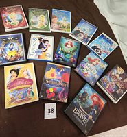 Photo showing all thirteen Disney DVDs arranged on a surface, displaying cover art of Tinker Bell, Frozen, Snow White, The Little Mermaid, Cinderella, Sleeping Beauty, Princess Enchanted Tale, and Brave.