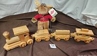 Wooden train set connected in a row with plush moose behind on brown fabric background.