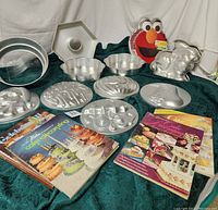 All cake pans and cookbooks displayed on green fabric, showing shapes, sizes, and covers