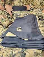 Photo showing folded blue bed skirt with subtle texture and slight sun fading on one side, laid on floral comforter.