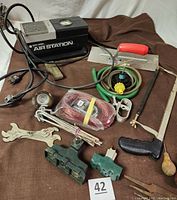 Overall photo of the entire lot showing Black & Decker Air Station compressor, pool cover winch kit components, green hoses, hand tools, and hardware.