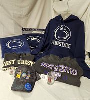 Photo showing Penn State hoodie, pillows, West Chester hoodies, shot glasses and NCAA hat.