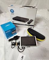 Photo showing four main electronic items: Onn DVD player with remote in white box, Amazon Echo Dot smart speaker boxed, Garmin Nuvi GPS device with cables and dashboard mount, and black and yellow carrying case for Mighty Sight LED magnifying eyewear.