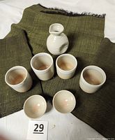 Front view of the yaki ware sake set arranged on a green placemat, showing 4 small cups, 1 pitcher, and 2 small bowls