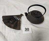 Photo showing the cast iron tea kettle with metal handle and lid alongside the Japanese fan-shaped iron pot stand on a white fabric background.