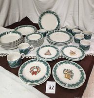 Photo showing full set including stacked plates, mugs, bowls, and featured decorative luncheon plates with different Christmas designs arranged in front.