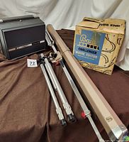 Full lot showing Bala Challenger movie editor with original box, tripods, and Da-Lite screen casing tube on brown blanket backdrop.