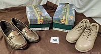 Both pairs of SAS shoes shown next to their original boxes on a brown fabric background.