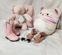 Full view of all items: pink cowgirl boots, plush baby blanket set, squishmallows plush toy, pink sandals, and sunglasses
