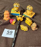 Overview of all Garfield collectibles in the lot including figurines, pencil toppers, sharpener, and pin