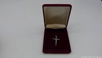 Front view of the crucifixion pendant inside the open burgundy velvet jewelry box with a cream interior.