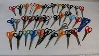 Photo showing a wide spread of 39 assorted scissors arranged on a table with different handle colors and blade sizes.
