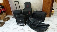 Photo overview of seven black assorted bags including luggage and duffle