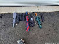 Photo showing all 9 umbrellas laid out horizontally on gravel surface by a garage door. Various colors and handle styles visible.