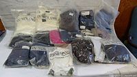 Photo of assorted women's clothing items mostly in plastic bags laid out on table, brands visible include IN' VOLAND and meaneor