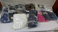 Photo showing multiple plastic-packaged women's clothing items in various colors such as navy, white, pink, gray, and black with visible Finejo branding on packaging.
