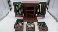 Wooden jewelry box with two side doors open displaying hanging necklaces, and three drawers open showing bracelets and rings