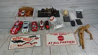 Wide view showing all items in lot: toy cars, motorcycle, phone, calculator, phone cases, novelty signs, baseball, wooden figure.