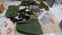 Full lot showing various military backpacks, bags, pouches, and cases on a patterned carpet.