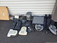 Photo showing assortment of Polycom conference equipment, printers, monitor, keyboards, and mounting bracket arranged outdoors on pavement.