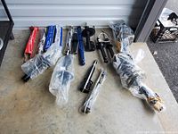 Assorted vehicle shock absorbers laid on concrete floor, various types and sizes, some wrapped in plastic.
