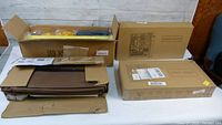 Photo showing several cardboard boxes containing parts for the mobile portable storage cabinet, including folded brown fabric panels and boxed assembly pieces.