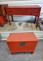 Front view of dressing vanity table with five drawers and matching wooden dower chest closed with metal latch, both in red-brown finish.