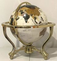 Front angle of the rotating globe on brass tripod stand with claw feet, showing continents map and supporting brass ring.