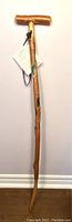 Full view of the wooden walking stick showing entire length and T-shaped handle against a wall.