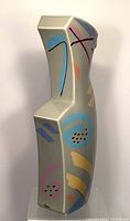 Side angled view showing colorful abstract brushstroke patterns on the matte gray angular ceramic vase with artist signature near base.