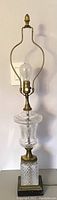 Full frontal view of one lamp showing harp, finial, crystal body, brass accents and marble base