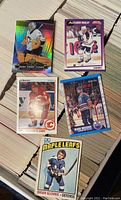 Five assorted cards including Upper Deck Marc-Andre Fleury, Topps Alexander Mogilny, O-Pee-Chee Al MacInnis, O-Pee-Chee Mark Messier and Topps Brian Glennie on stacks of cards