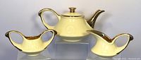 Front view of the pearl yellow teapot with matching creamer and sugar bowl on clear risers, showing 22k gold trim on handles, spouts, rims, and lids.