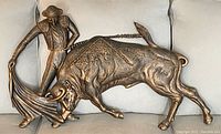 Full front view of the metal wall hanging showing the matador and bull in bronze finish against a neutral background.
