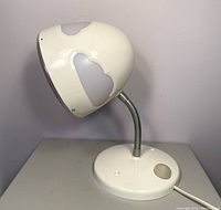 White rounded desk lamp with opaque cloud decorations on shade, flexible metallic neck, and round base with push button switch on side