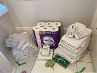 Full view of the lot with toilet paper packs, soap bars, and towels stacked on bathroom floor.