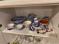 Shelf holding eight pottery items including bowls and creamers primarily in blue and white patterns, plus a wood and stone bead necklace.