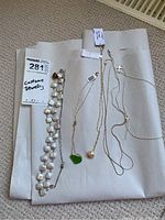 All seven pieces of costume jewellery necklaces laid out on brown paper background showing different styles including freshwater pearl necklace and chain necklaces with pendants.