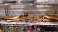 Photo of wooden cutting boards, jam jar, wooden and metal spoons, small ceramic bowl and a cookbook titled 'Krillz'. Items arranged neatly on wire shelf.