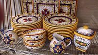 Full view of the ceramic dinnerware set on metal shelving wire rack including plates, bowls, creamers, jar and serving platters.