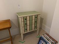 Front view of the dresser showing three drawers with round handles and vertical brown stripes, painted in distressed green and cream.