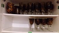 Two white shelves holding leopard-print glassware: top shelf with two vases and eight glasses, lower shelf with six glasses