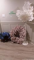 Full view of untested white fabric shade floor lamp with floral wreaths and blue hydrangea near wall