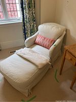 Photo showing full lounger chair with checkered fabric upholstery, pink throw pillow, and white blanket in living room setting.