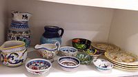 Wide view of the pottery lot showing jugs, creamers, bowls, and plates with colorful hand-painted designs