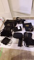 Overview of multiple black purses laid on floor, some with chain straps, various textures including leather, sequins, and feathers.